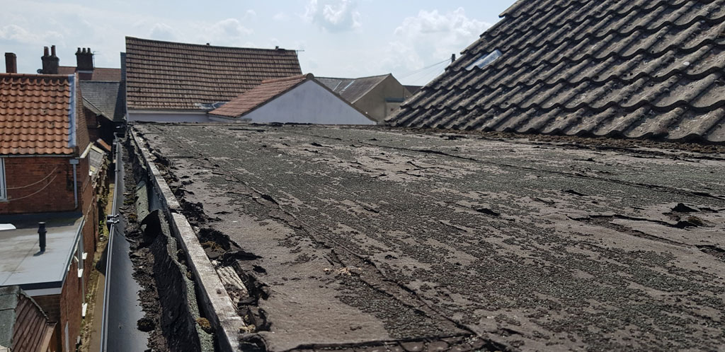 A weathered rooftop is visible, showing signs of wear and peeling material. The scene includes neighboring rooftops and a clear sky in the background.