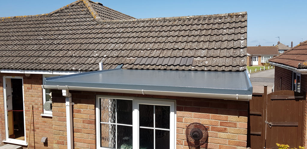 A flat roof extension is visible on a brick house, adjacent to a sloped tiled roof. The scene is set under a clear blue sky, showcasing the home's exterior features.