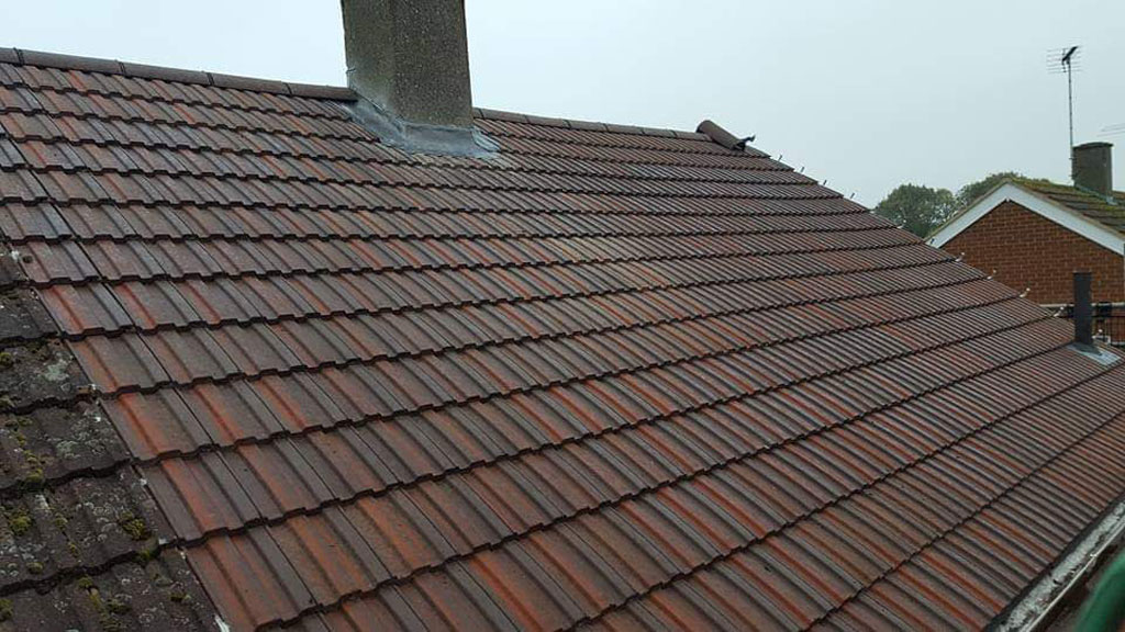 A sloped roof covered with red clay tiles is visible, featuring a chimney at the top. The tiles show signs of weathering and some moss growth, indicating age and exposure to the elements.